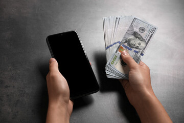 Woman with money and smartphone at grey table, closeup