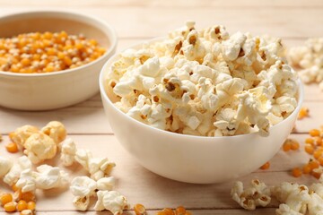 Tasty popcorn and corn kernels on white wooden table, closeup