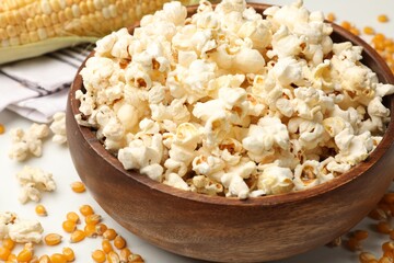 Tasty popcorn and corn kernels on white table, closeup