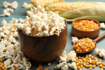 Tasty popcorn and corn kernels on blue wooden table, closeup