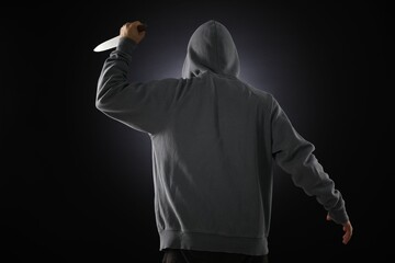 Criminal with knife on dark background, back view