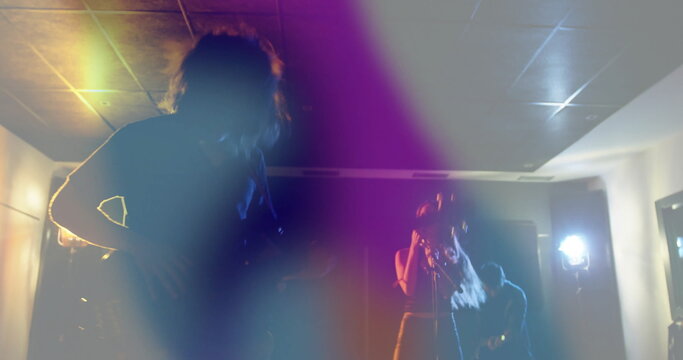 Performing musicians strumming guitars and singing on stage under colored lights, with mic stand