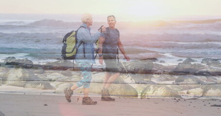 Obraz premium Using trekking poles couple hikers walking along beach at sunrise, with backpacks