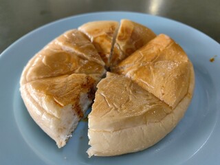 Close-up of a round bun bread filled with savory filling, sliced into pieces and served on a blue plate.