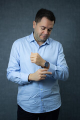 Office worker getting ready for work, buttoning his shirt cuffs. Ideal for corporate business, career, office work, employment. Studio portrait with copy space on blue background.