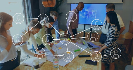 Collaborating business team of seven leaning over table in office, with plans and network overlay