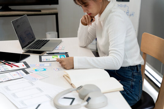 Adult Asian woman UX UI designer developing mobile application wireframes digital product interface design office workspace focused creative thinking