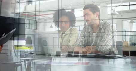Collaborating office professionals reviewing data on laptop at glass office interior, with notebook