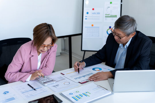 Asian adult business professionals calculating financial data analyzing market reports collaborating corporate office setting for strategic planning development - Powered by Adobe