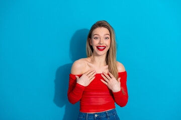 Fototapeta premium Cheerful young woman in vibrant red top posing against a bright blue background with radiant happiness and charm