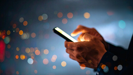 Man's hands using a smartphone with bokeh background, highlighting modern communication and technology
