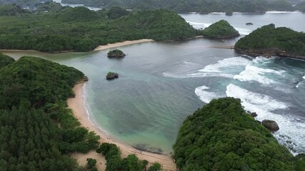 Beautiful aerial view of Teluk Asmara beach, Malang, indonesia. Waves with small waves among the islands scattered on the beach with green trees