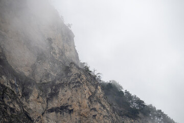Misty mountain slope shrouding rugged terrain, rocky landscape veiled by low hanging clouds, minimal greenery emerging