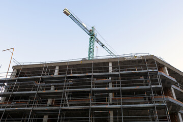 Construction crane working on top of building scaffolding with a clear blue sky in the background