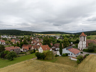 Scenic view of Waldachtal in Germany, showcasing the village, church, houses with red roofs, green fields, and forest under a cloudy sky