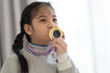 Celebrating winning fencing competition. Happy Asian girl fencer in fencing costume holding gold medal