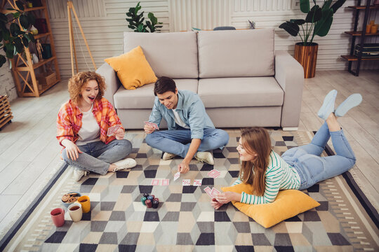Three friends joyfully playing cards and enjoying drinks in a cozy living room environment