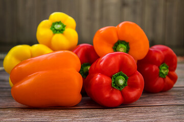 Red, yellow and orange bell peppers on rustic wooden background
