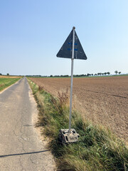 Triangular warning sign with back facing on a field, rural scene with traffic symbolism