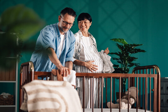 Happy couple preparing baby crib in modern nursery - Powered by Adobe
