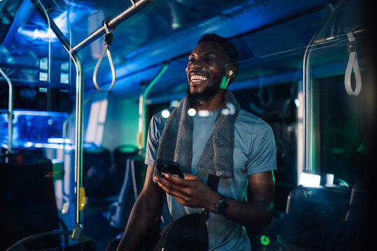 Happy sporty man using smartphone on night bus ride home