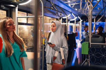 Muslim woman holding smartphone on a bus with nurse standing near