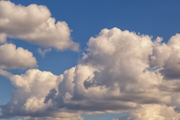 White clouds lined up in a row in blue sky close-up, cumulus white clouds in sunlight, fluffy textured clouds in the sky, cloudy background.