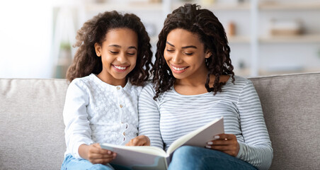 Family lifestyle, leisure activity concept. Joyful black mother and daughter reading book together at home, copy space. Beautiful african american family mom and child reading fairy tales