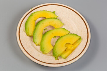Slices of avocado on saucer on gray surface, close-up