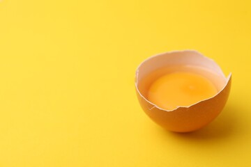 One broken chicken egg on yellow background, closeup. Space for text