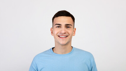 Fototapeta premium Portrait of handsome Caucasian young man in casual clothes smiling and looking at camera over light grey studio background. Friendly millennial guy with carefree smile posing