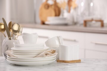 Different clean white dishware, cups and cutlery on marble table indoors