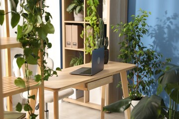 Stylish workplace with laptop on wooden desk and floral decor in office. Biophilic interior design