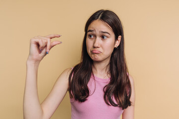 Fototapeta premium Young woman expressing disappointment with a small object against a plain background in soft lighting