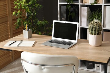 Stylish workplace with laptop, stationery and floral decor in office. Biophilic interior design