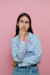 Fototapeta premium Young woman in a striped shirt posing thoughtfully against a pink background while contemplating ideas and expressions