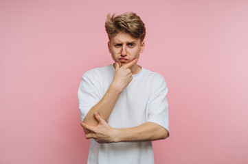 Young man with thoughtful expression poses against pink background considering alternatives in urban setting