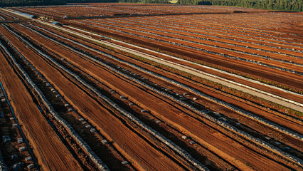 Aerial view of a large peat bog harvesting site with long parallel rows of extracted peat, wooden pallets, and covered stacks stretching across the landscape.