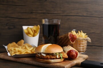 Different delicious fast food and cola on wooden table, closeup