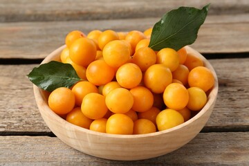 Ripe yellow cherry plums and leaves on wooden table, closeup