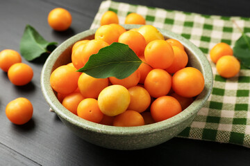 Ripe yellow cherry plums with leaves on black wooden table, closeup