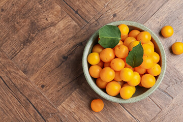 Ripe yellow cherry plums and leaves on wooden table, flat lay. Space for text