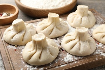 Uncooked khinkalis (dumplings) with peppercorns on wooden board, closeup
