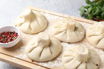 Uncooked khinkalis (dumplings), peppercorns and parsley on light table, closeup