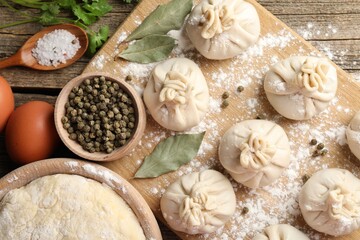 Uncooked khinkalis (dumplings) with peppercorns, flour, parsley and bay leaves on wooden table, flat lay