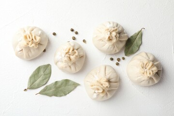 Uncooked khinkalis (dumplings) with peppercorns and bay leaves on white table, flat lay