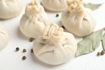 Uncooked khinkalis (dumplings) with peppercorns and bay leaves on white table, closeup