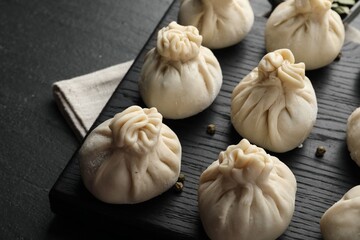 Fototapeta premium Uncooked khinkalis (dumplings) with peppercorns on black table, closeup