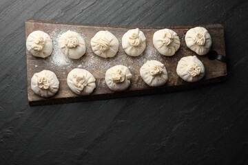 Uncooked khinkalis (dumplings) with flour on black table, top view. Space for text