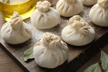 Uncooked khinkalis (dumplings) with flour and bay leaves on wooden table, closeup